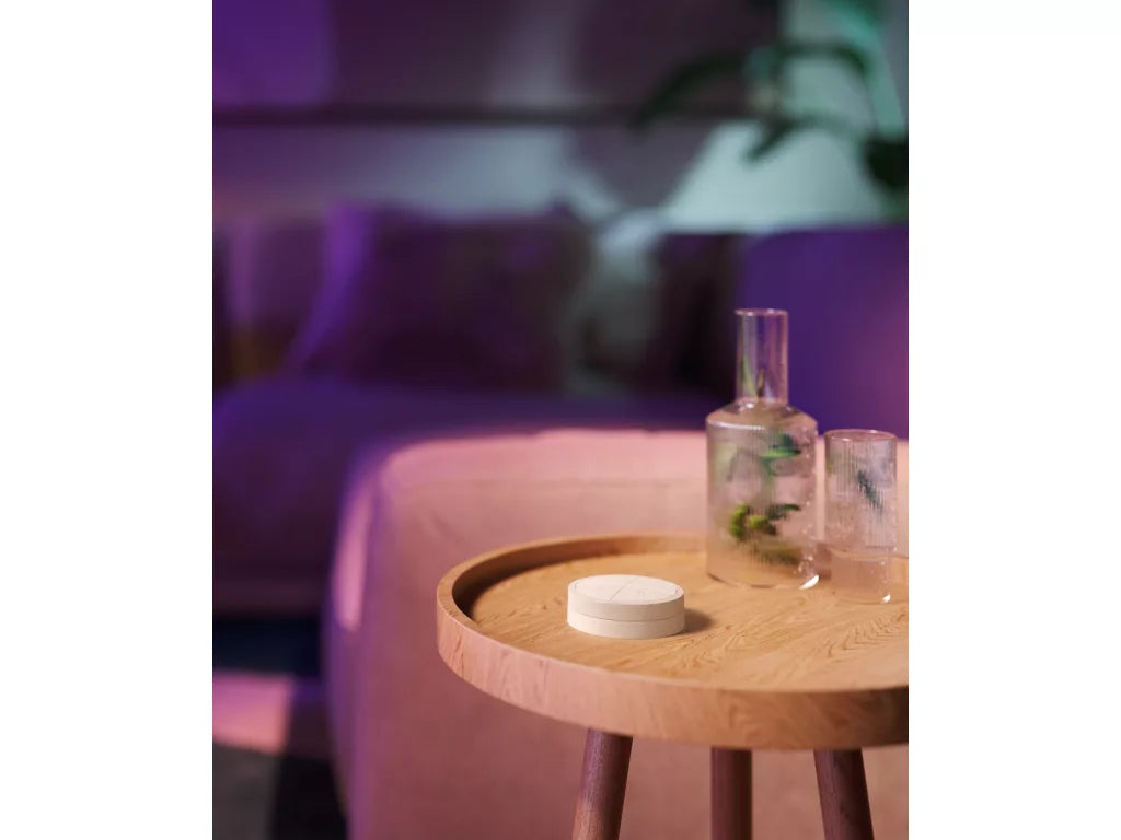 Philips Hue Tap Dial Switch on a wooden table with ambient lighting, designed for easy Hue light control.