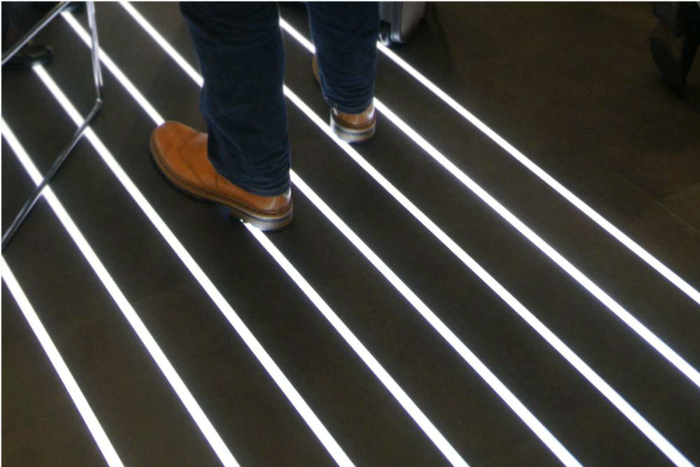 LED-profiili lattiaan asennettu, valoa erottuva lattia, jossa henkilö seisoo valkoisten LED-viivojen päällä.