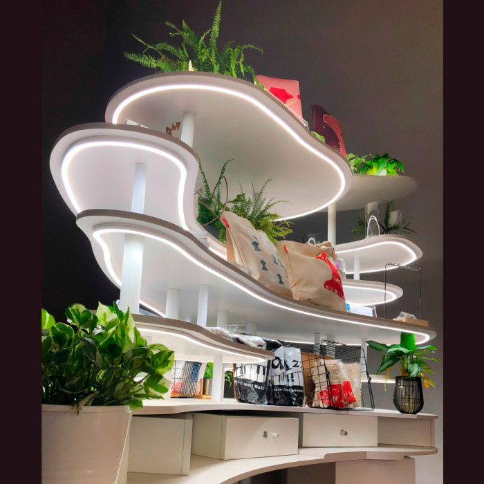 Tyylikäs LED-valonauha, joka valaisee modernia hyllyä kasvien ja laukkujen kera.