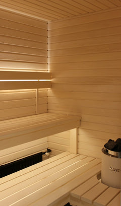 Pisteetön sauna LED-valonauha valaisee saunaa, jossa on puukuitupaneelit ja kivirakennelma. Täydellinen saunavalaistukseen.