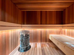 SAUNA LED-valonauha valaisee modernia saunaa, lämmin puupanelointi ja kivet saunakiukaassa.